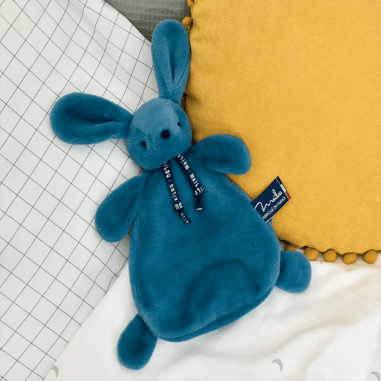 doudou plat lapin dorlotin bleu minéral maïlou posé sur des coussins